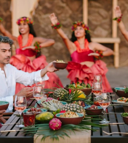 group of people enjoy dinner while women in red perform luau in the background