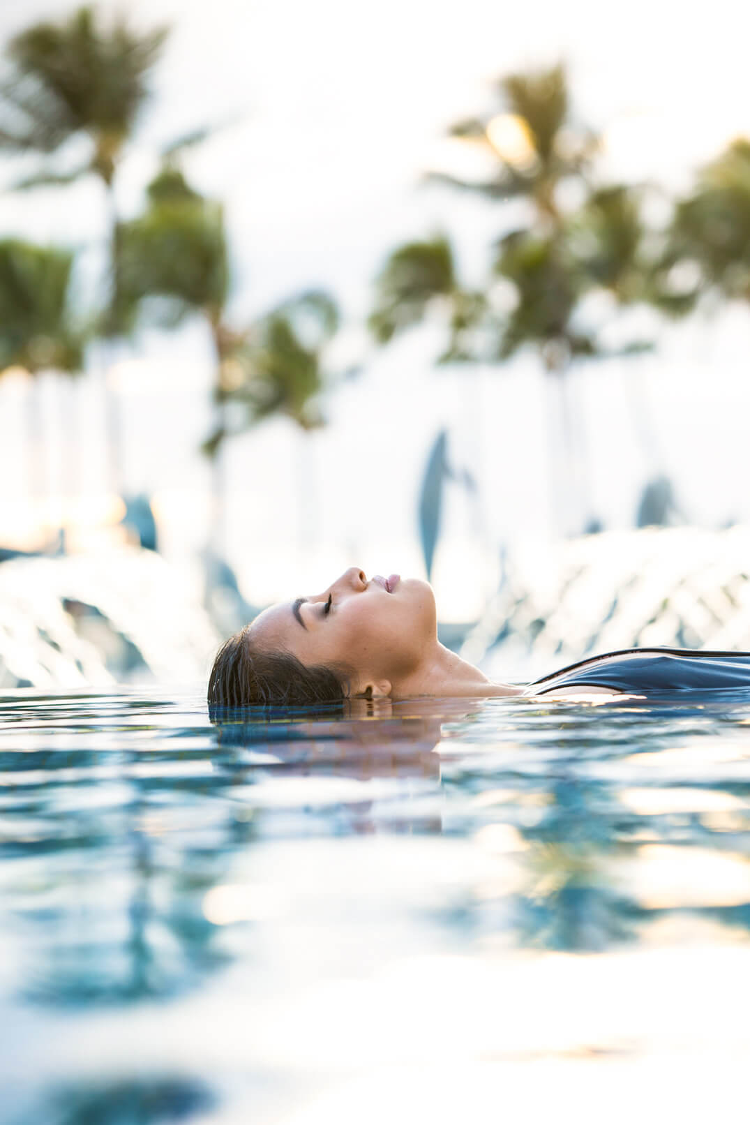 woman in pool floats on her back with palm trees in the background