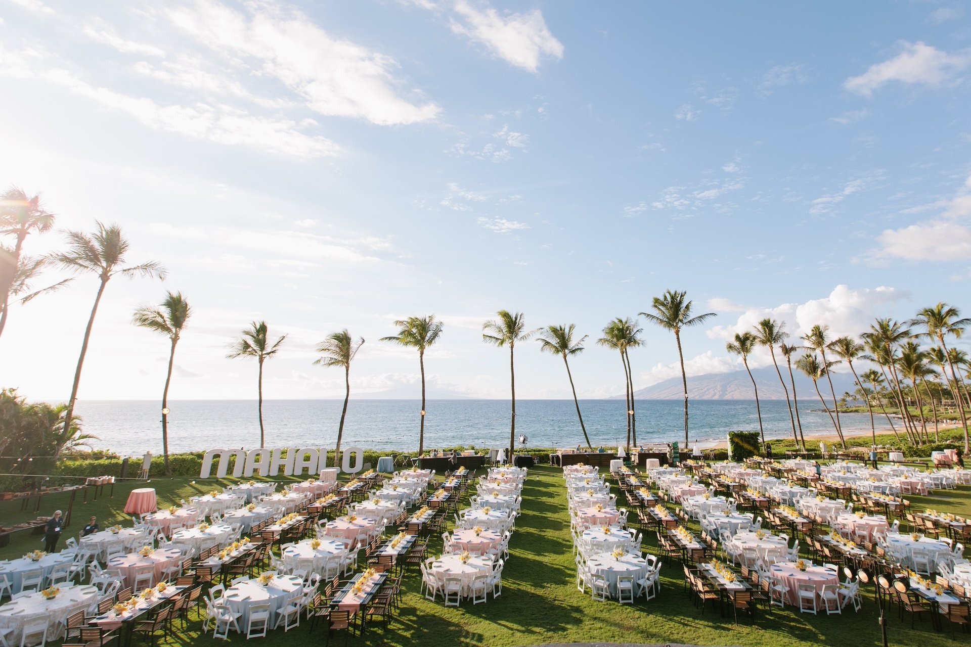 Many rows of banquet tables, set up on a lawn looking out on the ocean