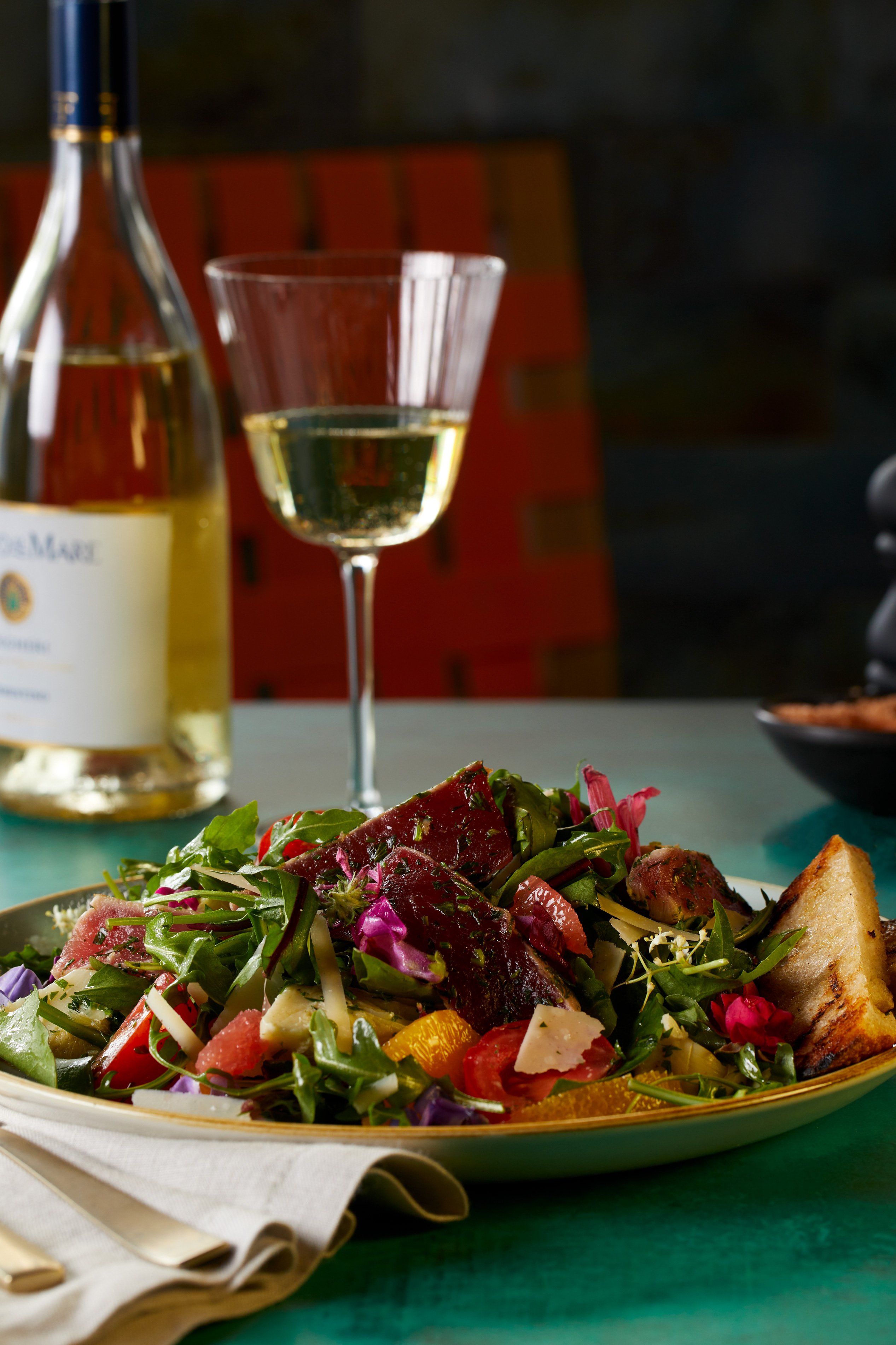 A delicious salad dish with a wine glass filled with white wine and a bottle