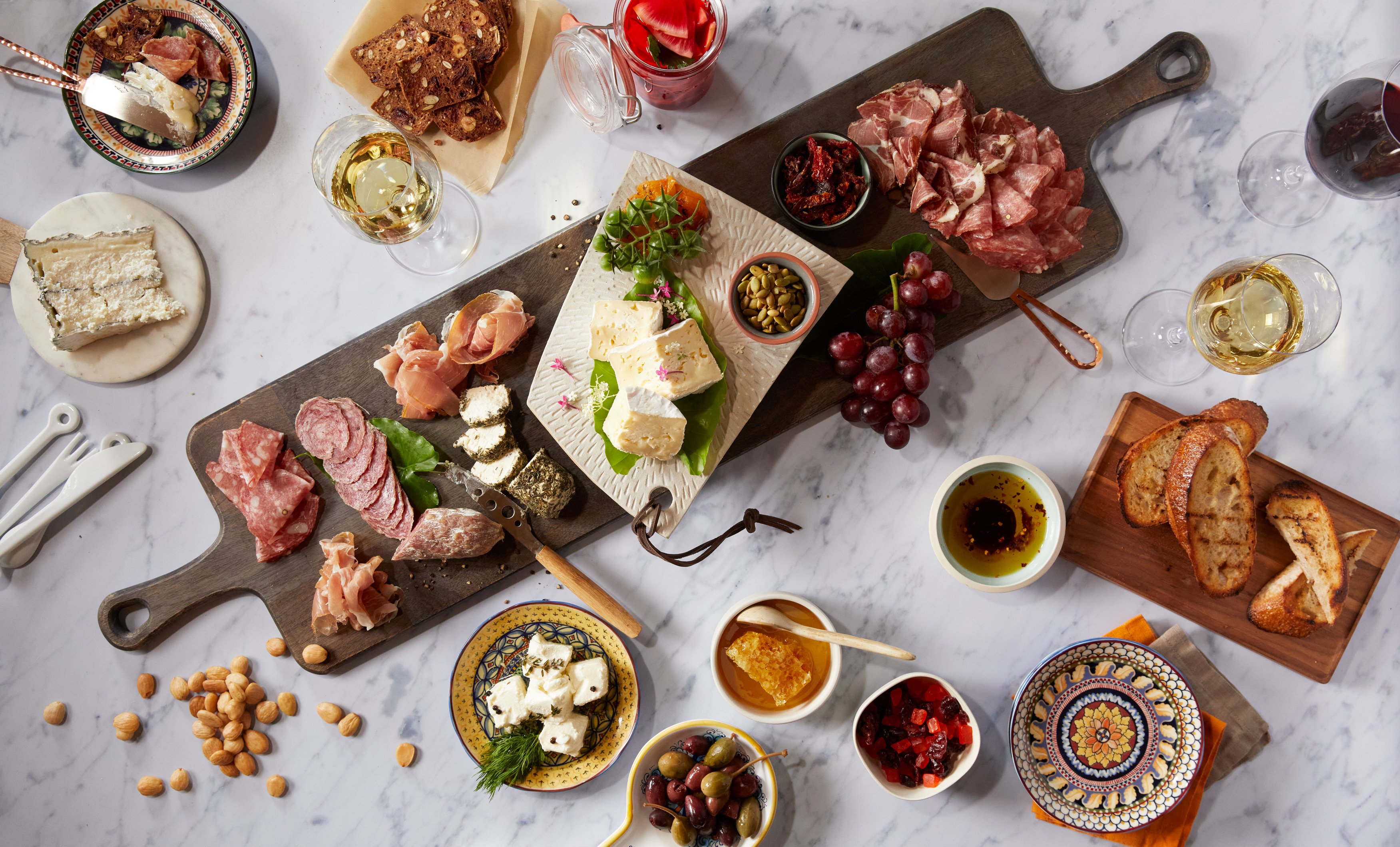 A charcuterie platter with side dishes on a white marble table  