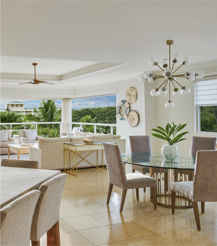 Interior living space of suite with chandelier, two tables, couch and large windows