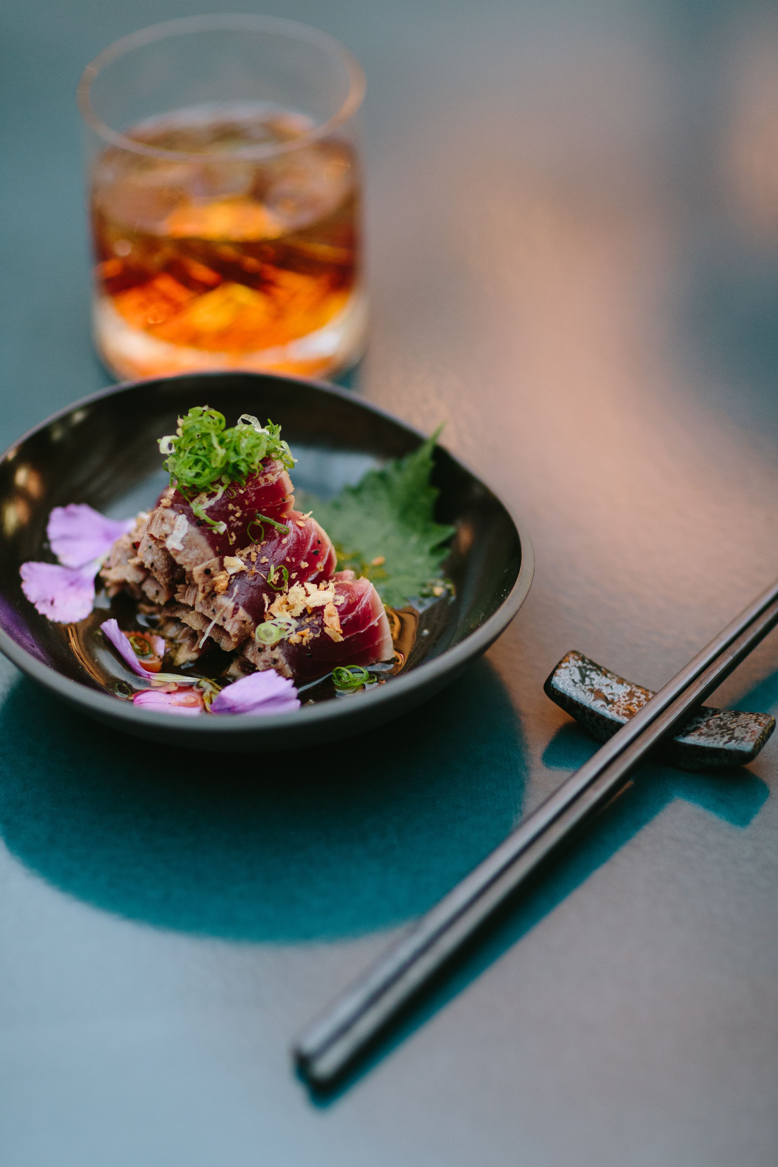 A sushi dish accompanied by chopsticks and a drink in a rocks glass