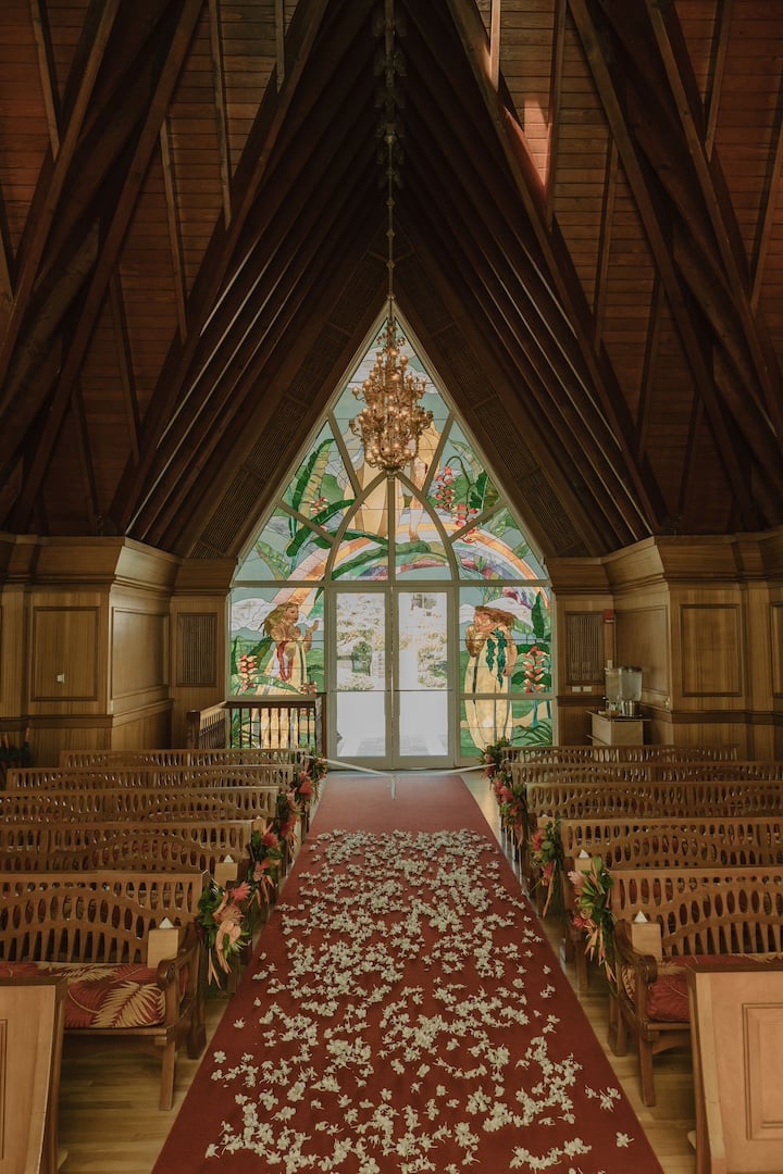 A wood chapel with an ornate arch and stained glass at the altar, decorated with flower petals