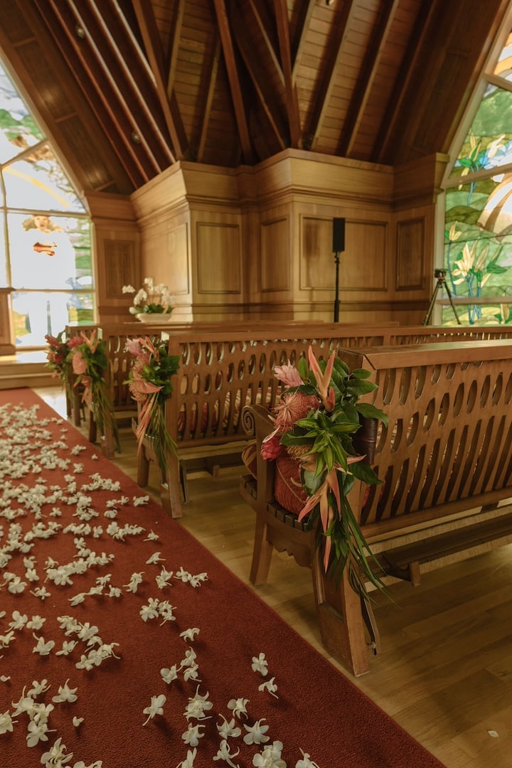 A sunlit wedding chapel with its red carpeted aisle covered in scattered rose petals