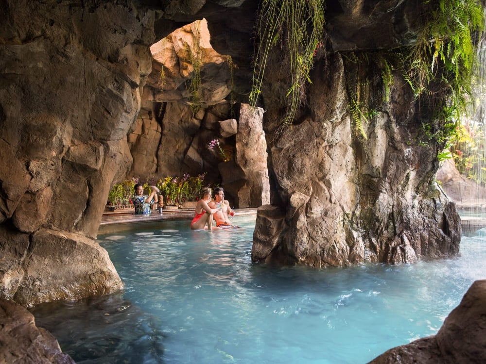 people swim up to grotto bar in a rocky cave while bartender stands behind the bar