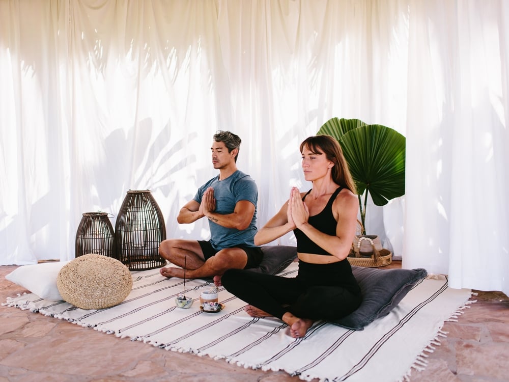 two people sit crosslegged on a striped blanket while meditating