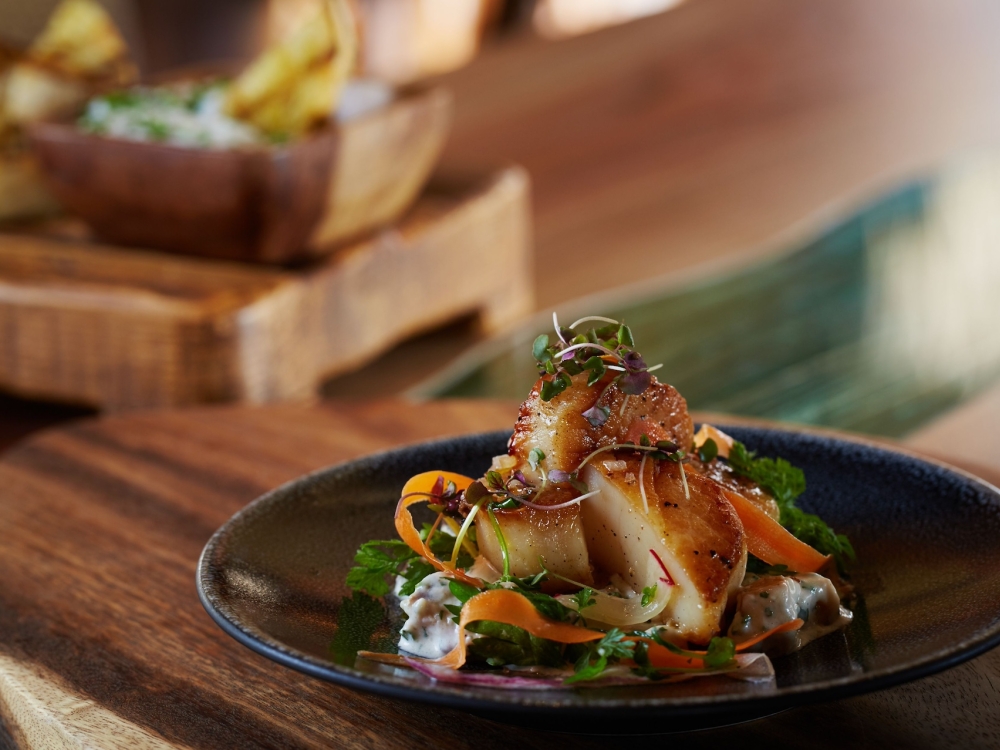 An ornate scallop dish on a wooden platter