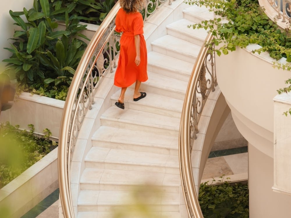 A woman in a red dress ascending a large spiral staircase