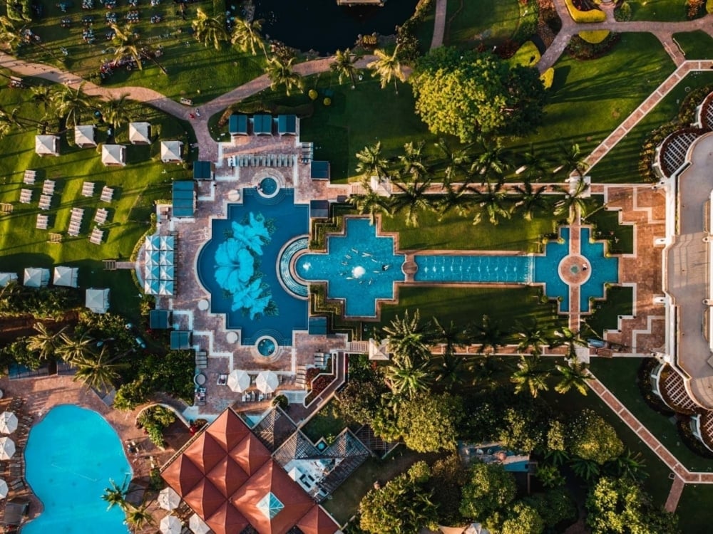 Aerial view of a resort grounds, with a large pool and garden next to villas