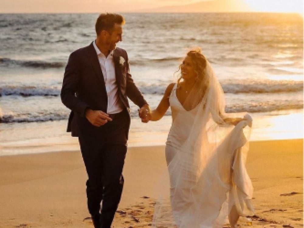 A bride and groom walk happily along the beach at sunset