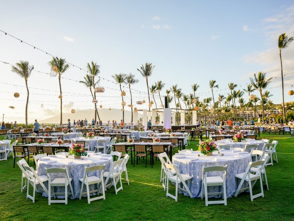 Outdoor banquet with white linen-covered tables under rows of lanterns