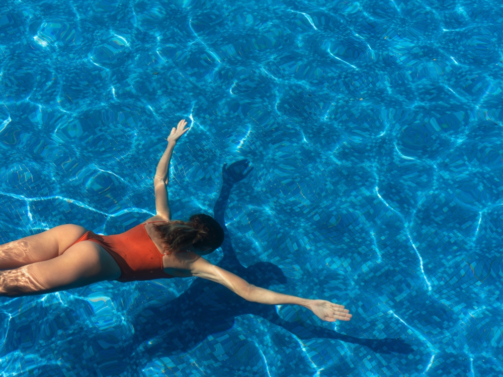 A woman in a red bathing suit dives into a clear blue pool 