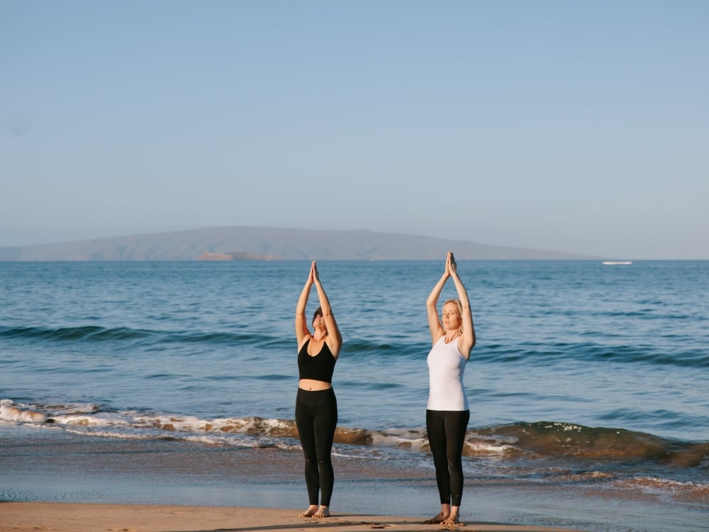 Two women practicing yoga on the beach