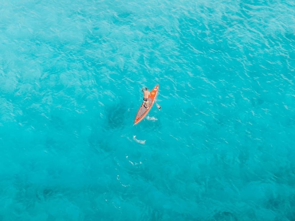 A stand up paddleboarder on a brilliant blue ocean