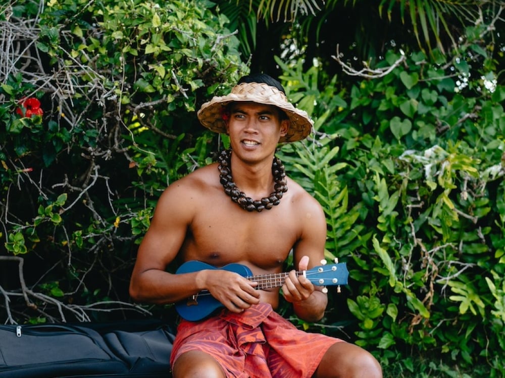 A ukelele player in traditional Hawaiian garb sitting in a garden