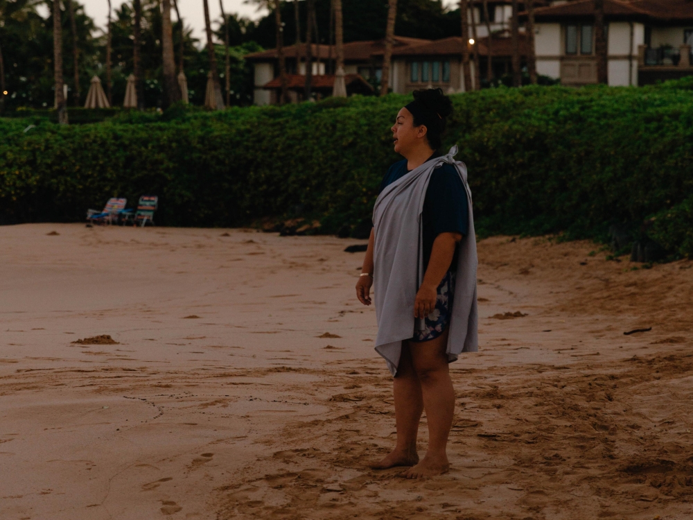 A woman standing on the beach reciting the E Ala E chant 