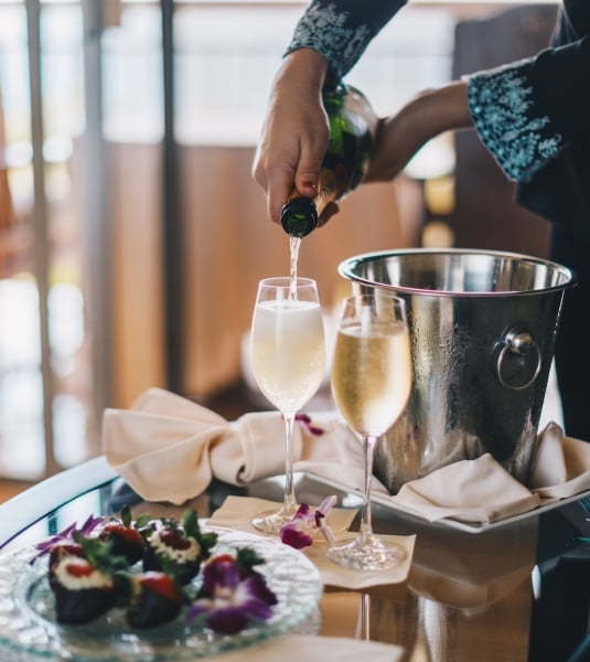 A person pour two glasses of champagne on a room service cart