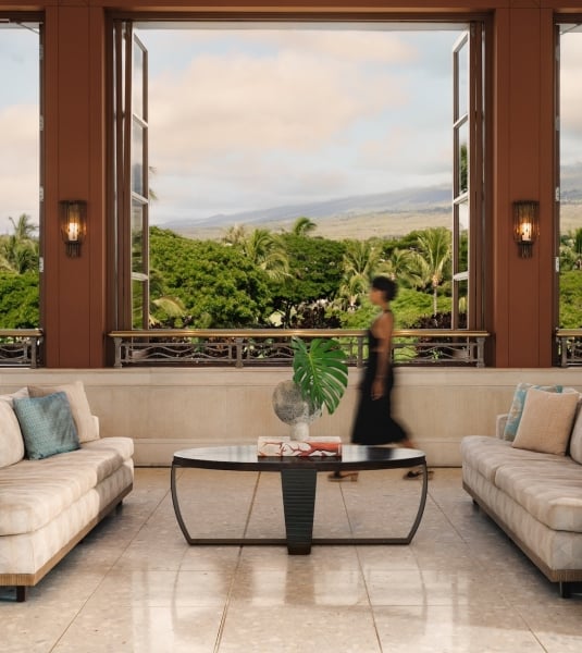 A woman traverses a lobby with grand bay windows looking out onto a green landscape