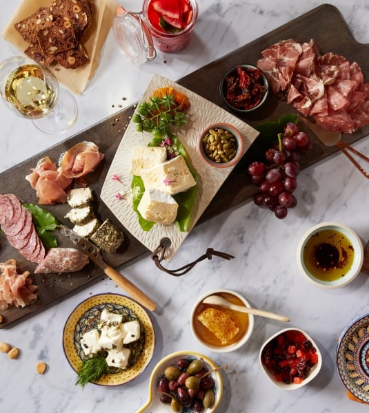 A charcuterie platter with side dishes on a white marble table  