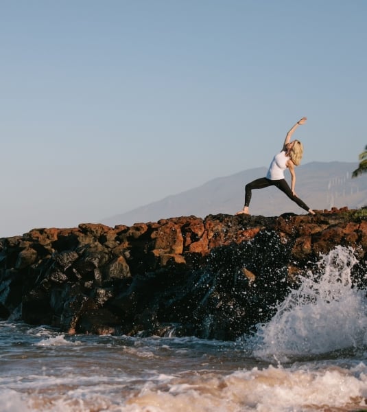 A woman doing yoga on a rock adjacent to the ocean