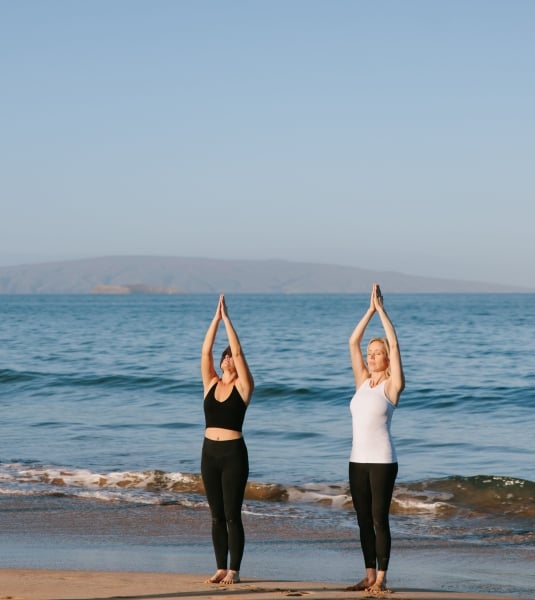 Two women practicing yoga on the beach