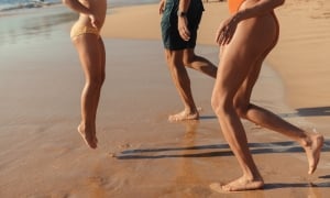 A detail of three people's legs as they jump and have fun on the beach