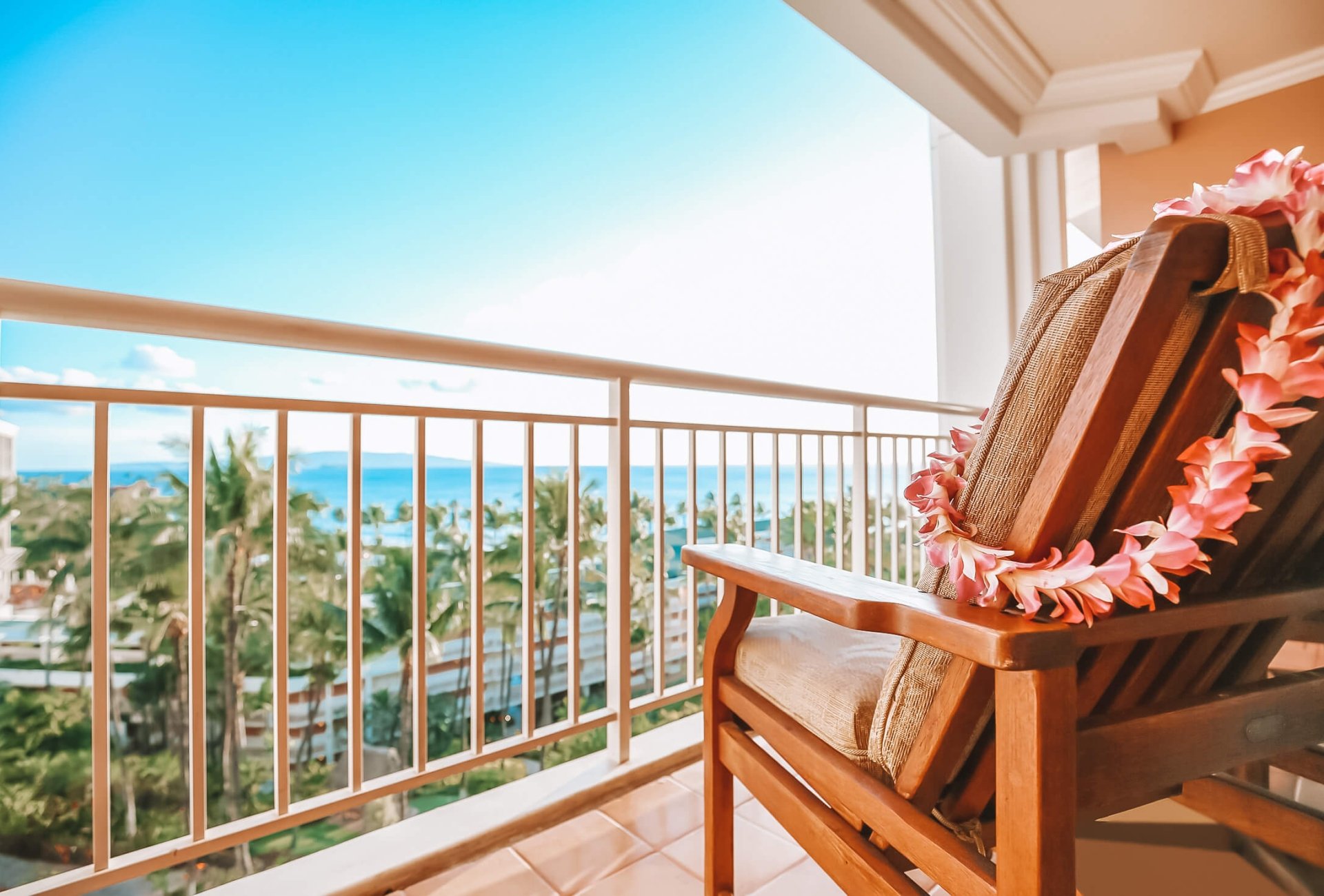 a chair with a pink lei hung from the back sits on a patio overlooking the blue sky and ocean