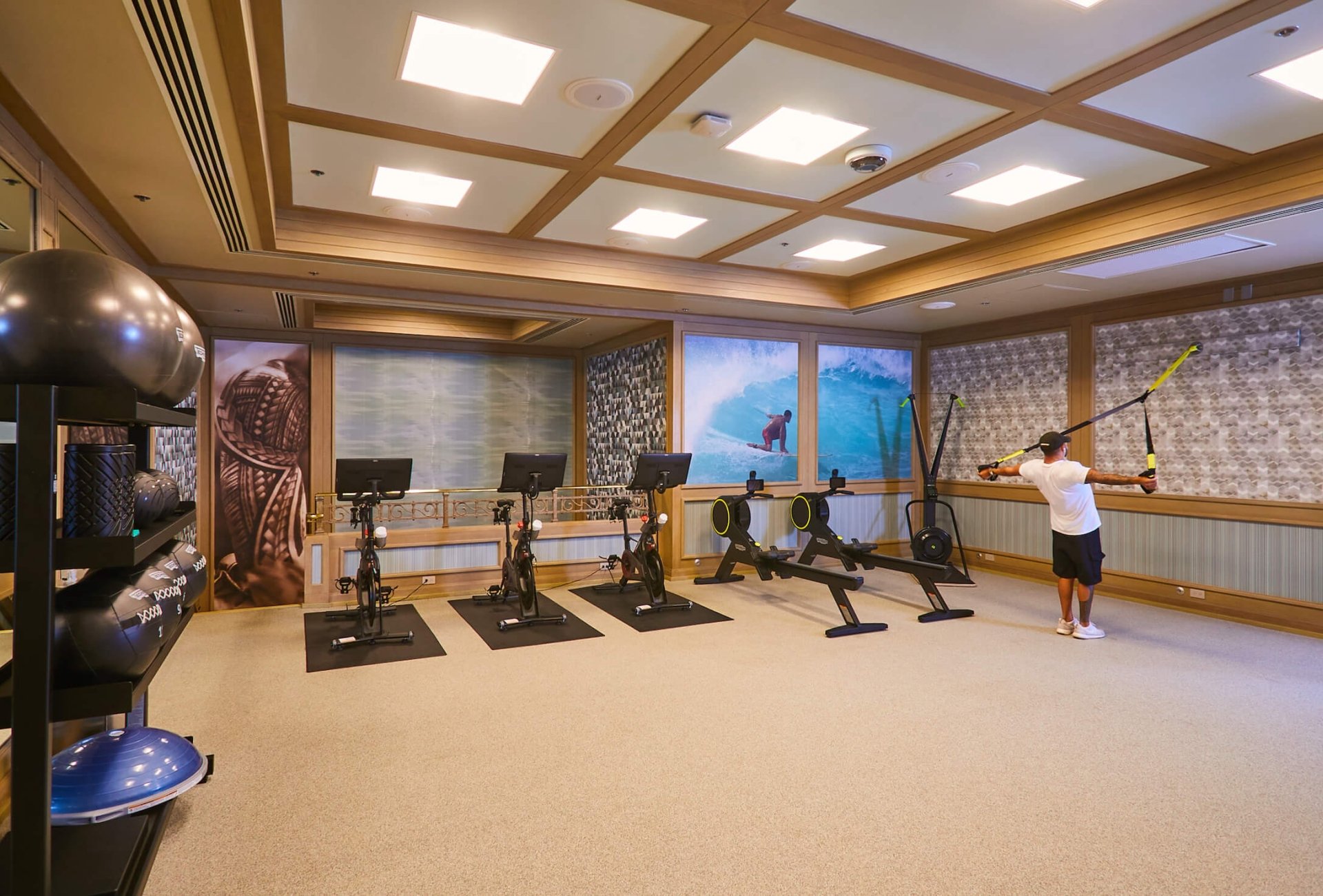 a well-lit interior of a gym with cardio machines and weights with a man uses a rope to workout