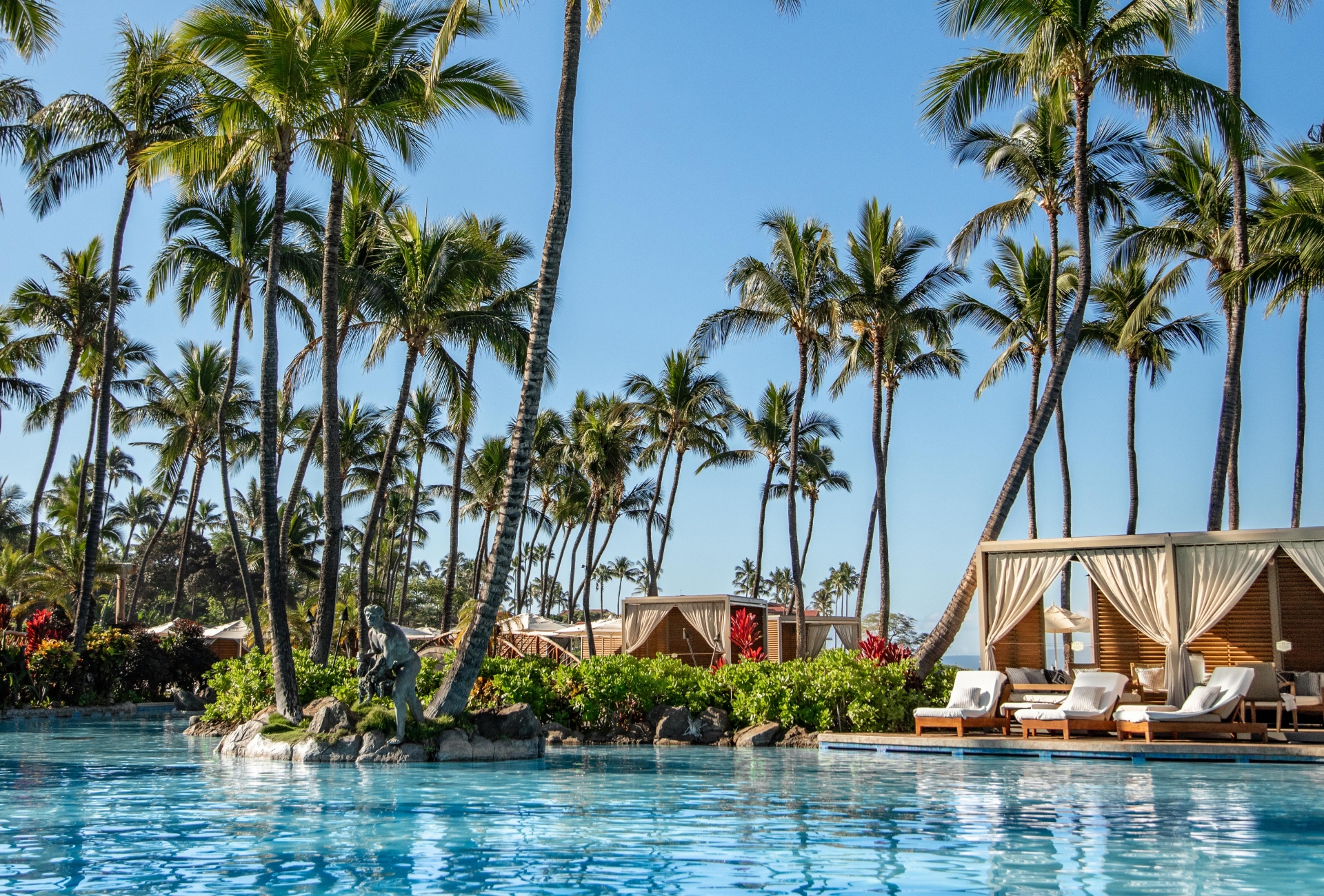 Sun falls on a sparkling blue pool lined with luxury cabanas and waving palm trees