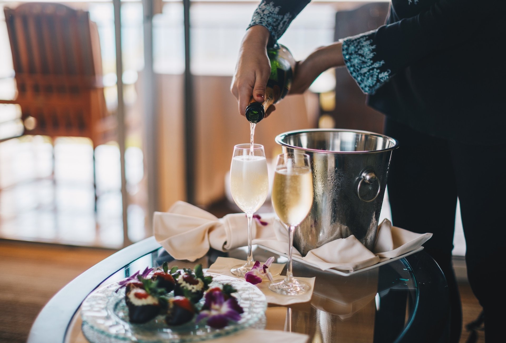 A person pour two glasses of champagne on a room service cart