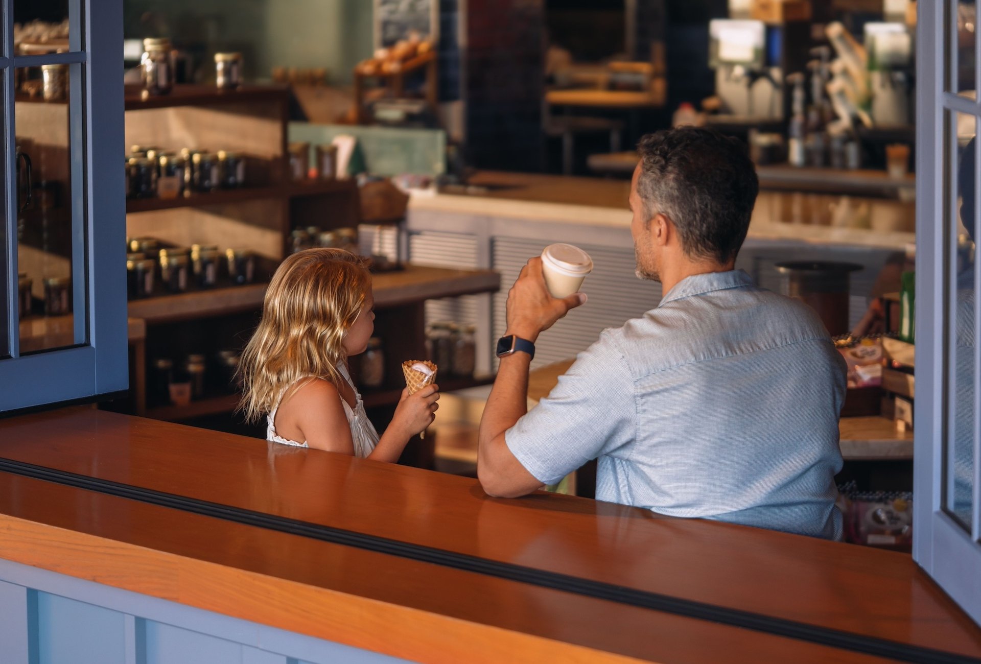 A man enjoys a coffee at a cafe while his daughter eats an ice cream cone