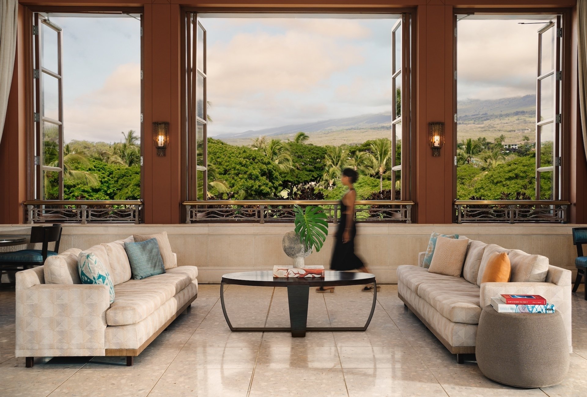 A woman traverses a lobby with grand bay windows looking out onto a green landscape