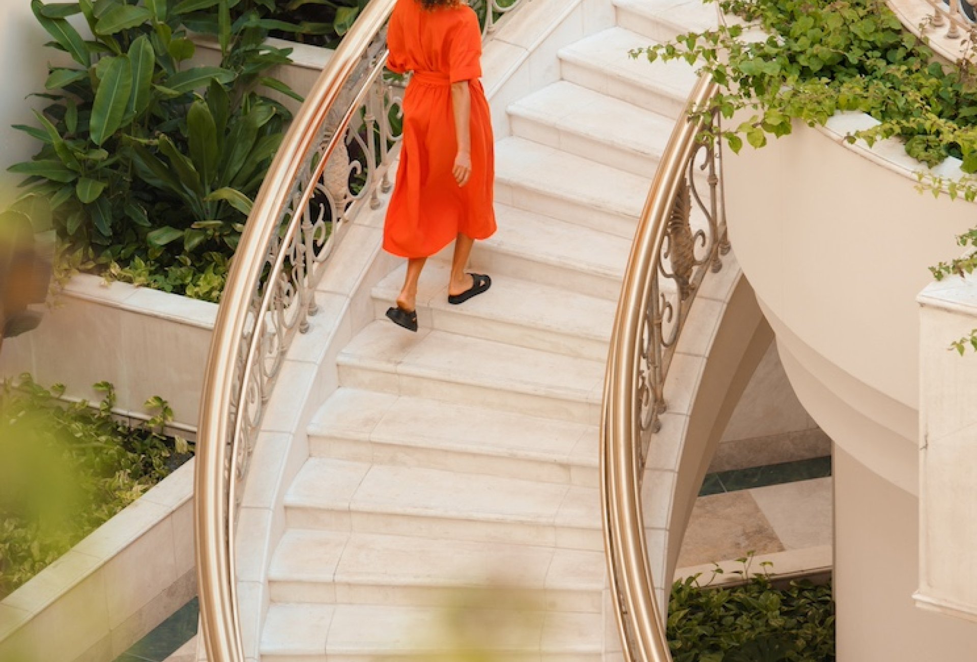 A woman in a red dress ascending a large spiral staircase