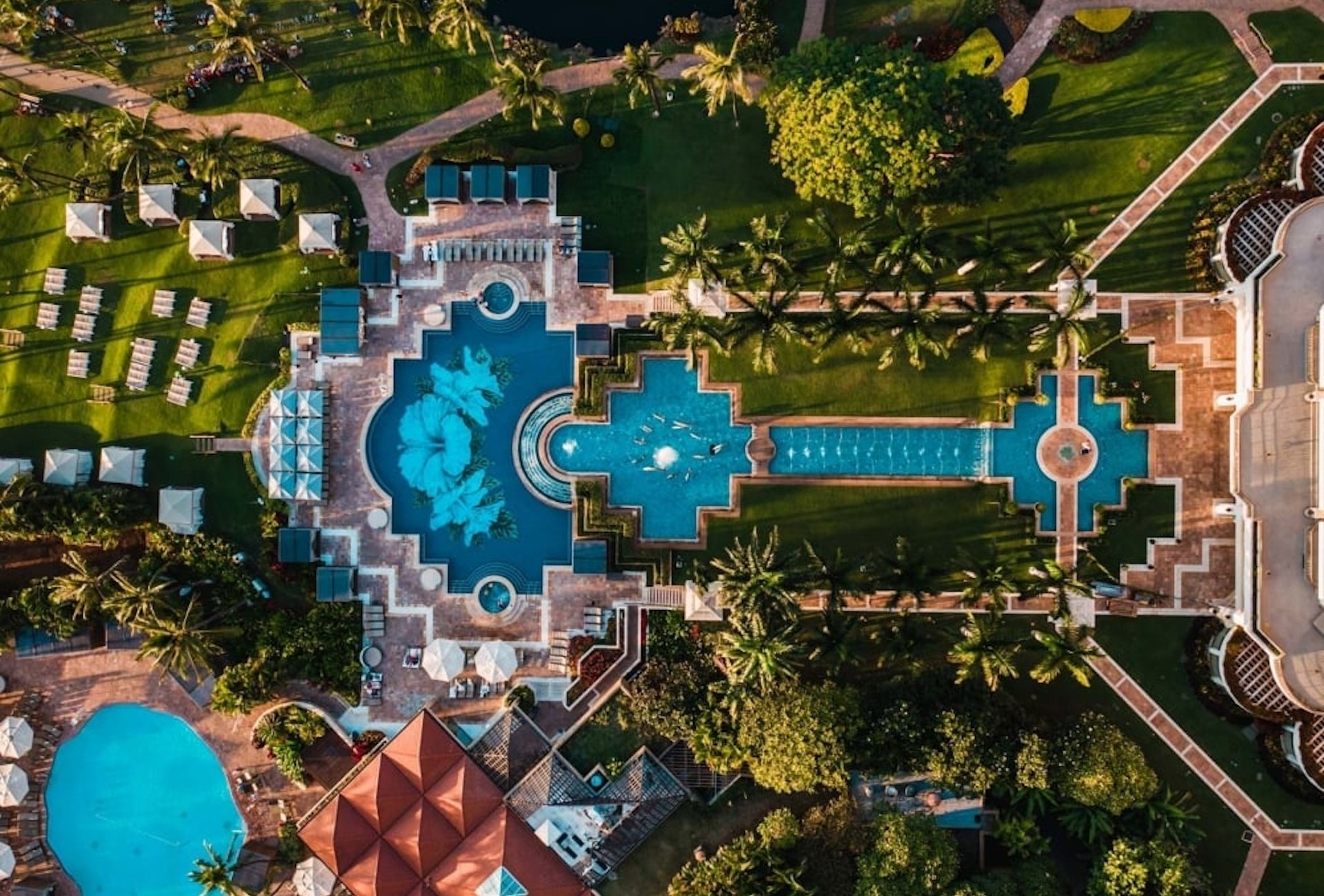 Aerial view of a resort grounds, with a large pool and garden next to villas