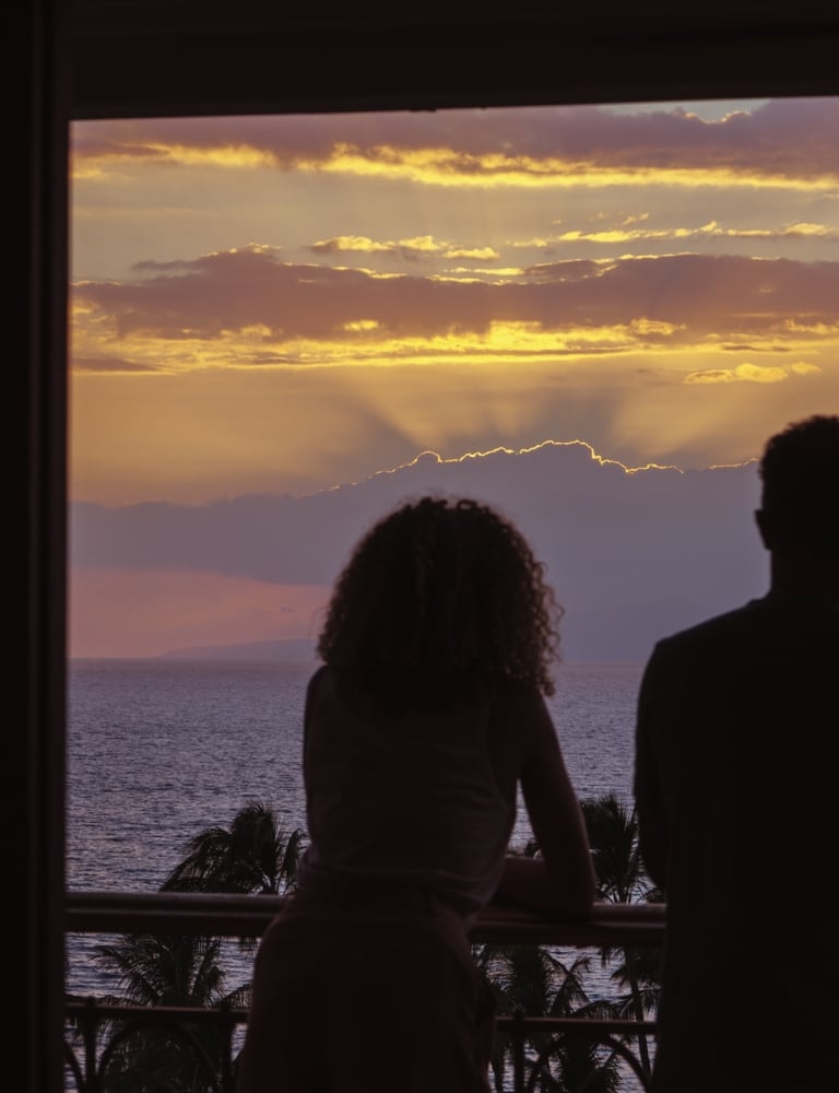 A couple looks out on the ocean from their balcony at dusk